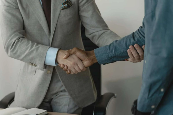 Two people shaking hands over a desk in a professional setting, symbolizing a successful business agreement or home closing.