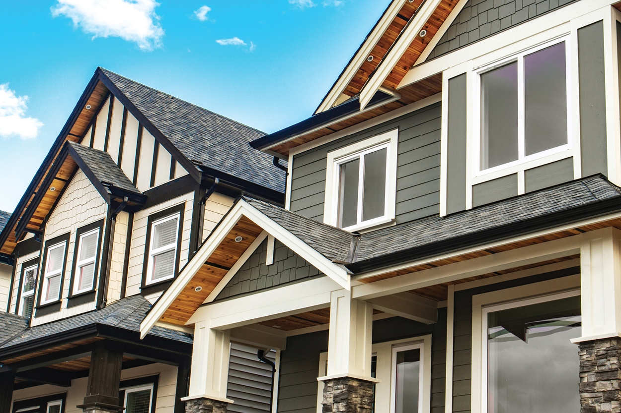 Craftsman style townhomes with gray and cream siding, white trim, stone-base columns, and a blue sky overhead